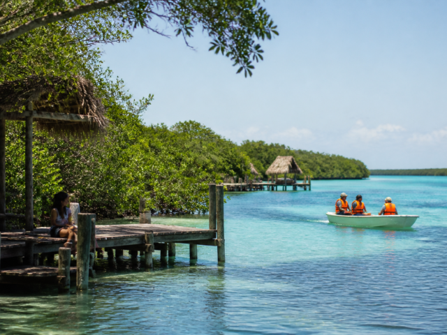 Lancha pequeña con chalecos salvavidas sobre la laguna de Bacalar, rodeada de manglar y agua azul clara.