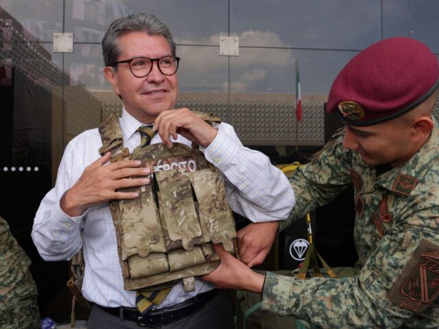 Ricardo Monreal ajusta un chaleco táctico con ayuda de un militar durante una exhibición.