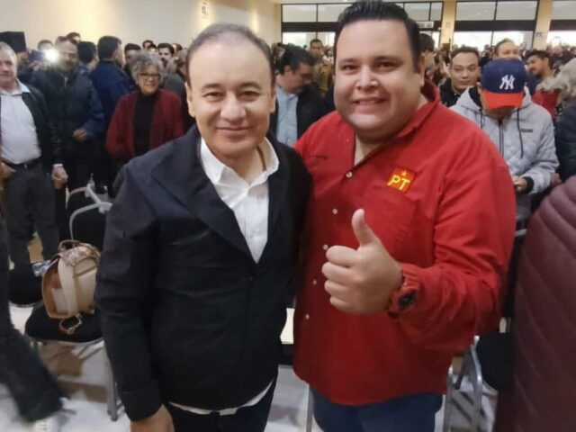 Dos asistentes posan durante un encuentro político en Hermosillo; uno viste una camisa roja con el emblema del PT
