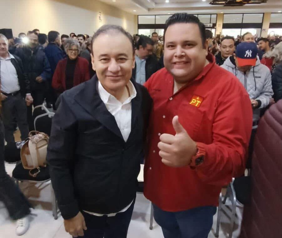 Dos asistentes posan durante un encuentro político en Hermosillo; uno viste una camisa roja con el emblema del PT